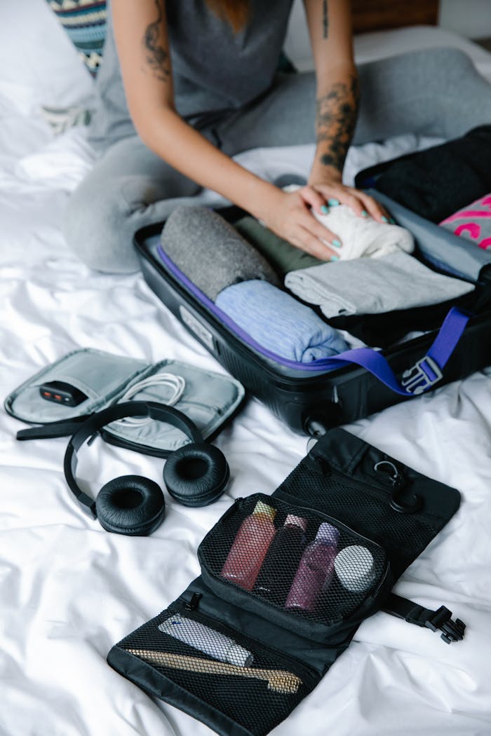 Home Person organizing suitcase with clothes and toiletries on bed, preparing for travel.